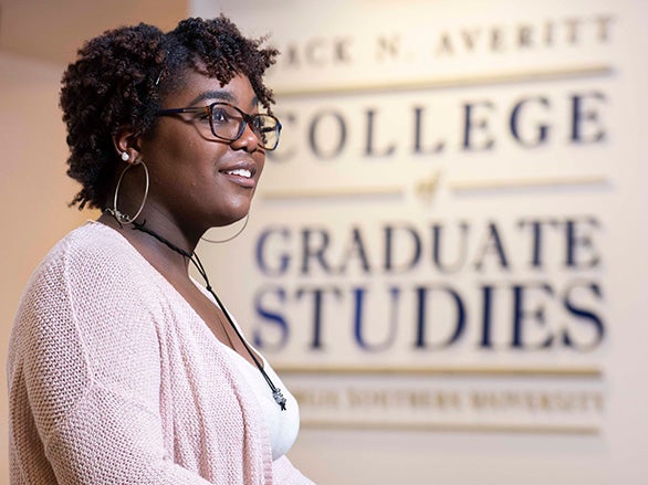 A student wearing glasses stands near a sign for Georgia Southern's College of Graduate Studies.