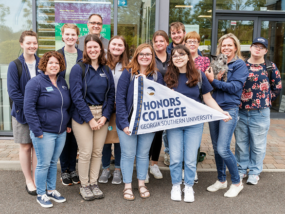 A group of students from Georgia Southern's Honors College stand outdoors with a pennant