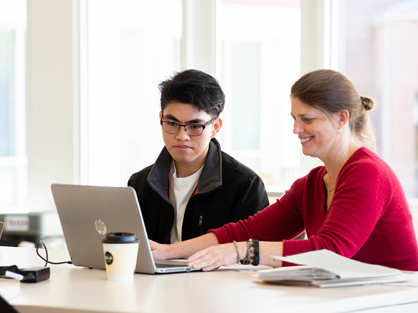 Sitting in front of a laptop, an instructor from Georgia Southern's M.Ed. in Higher Education Administration program meets with a student about their capstone project