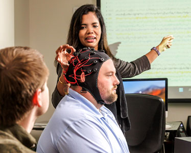 A faculty member from Georgia Southern's College of Behavioral and Social Sciences assesses a test subject wearing a helmet that analyzes brain function