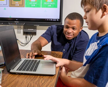 A student teacher from Georgia Southern's College of Education assists an elementary grade student who's using a laptop