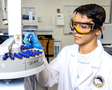 A student from Georgia Southern's College of Science and Mathematics wearing safety goggles and a lab coat organizes test tubes in a research laboratory