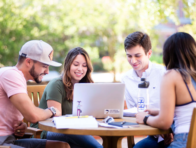 Four Georgia Southern students sit around a table with a laptop for an outdoor study session.