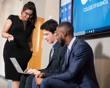 Three students from Georgia Southern's Parker College of Business wearing business dress review information on a laptop.