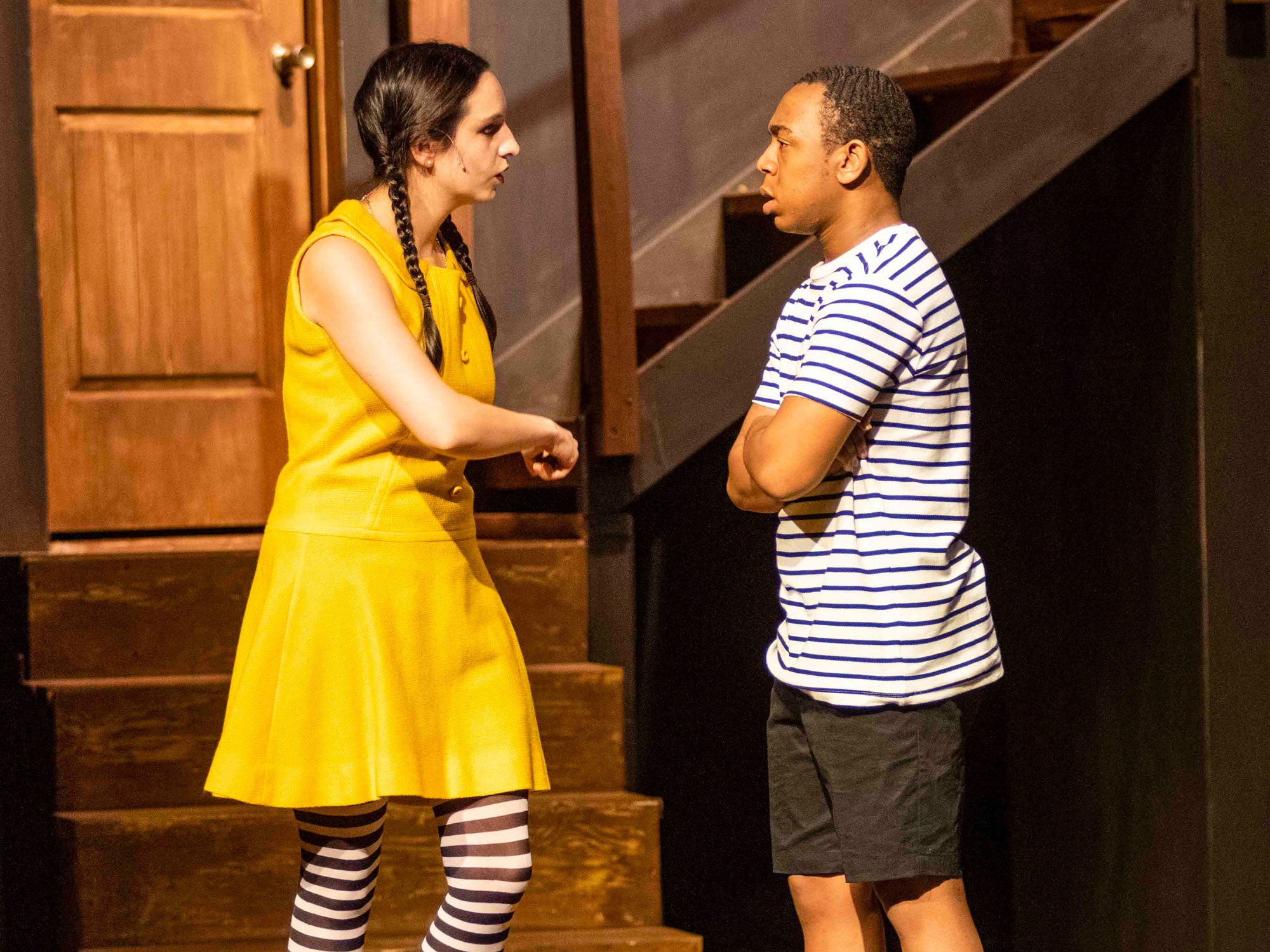 Two Georgia Southern B.A. in Theatre students in costume stand near set pieces for stairs and a door during a production