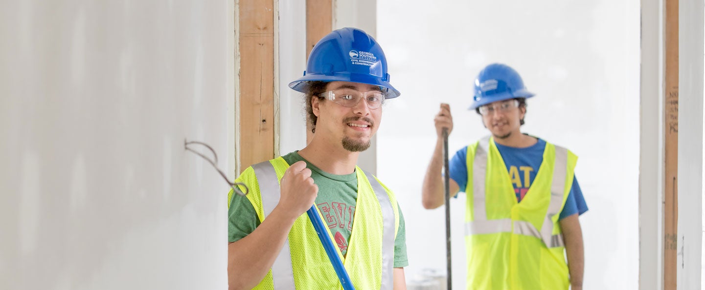 Two B.S. in Construction Management students from Georgia Southern stand inside a partially completed building while wearing hard hats and hi-vis vests