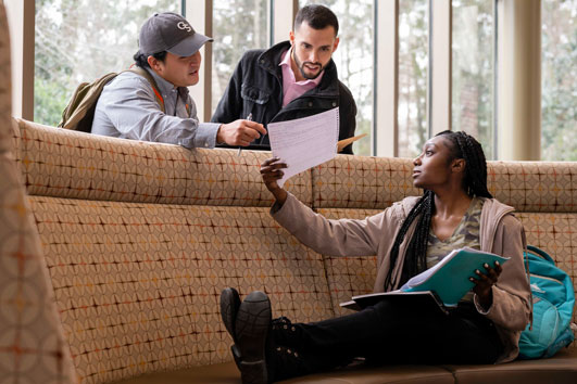 Three students from Georgia Southern's College of Behavioral and Social Sciences review a form in a common area