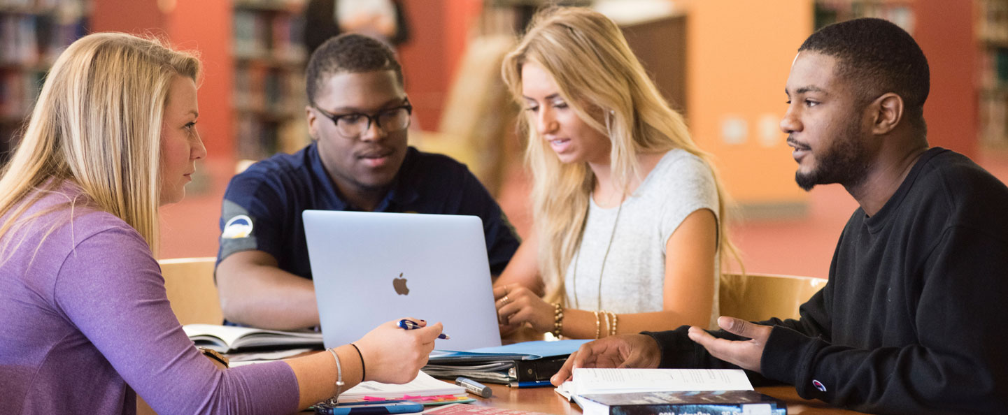 Sitting around a table with a laptop in a campus library, four students from Georgia Southern's College of Graduate Studies collaborate on a project.