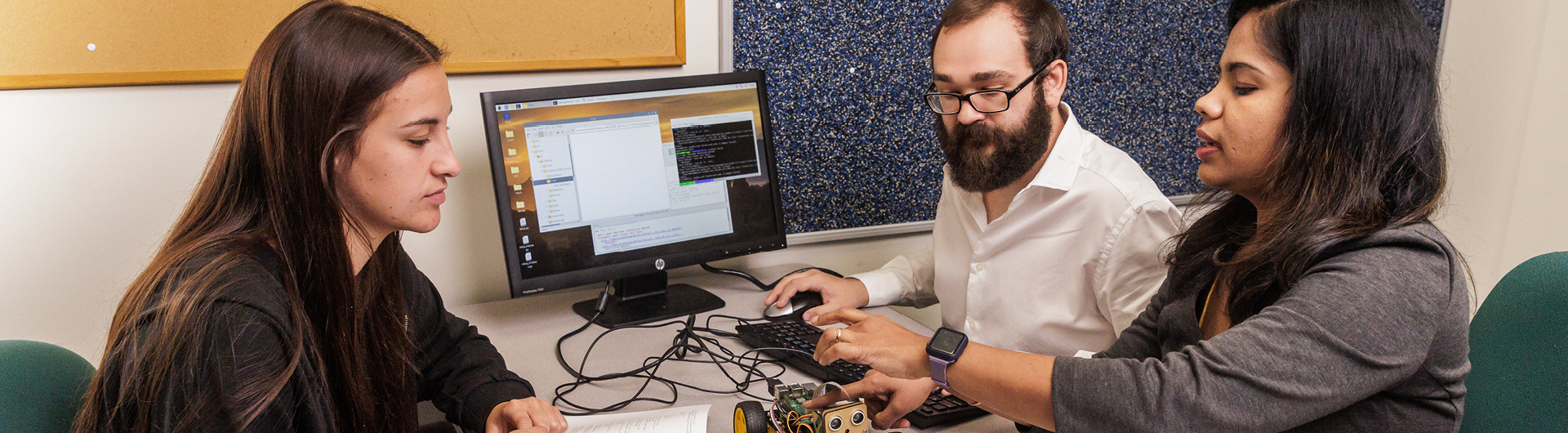 Two students from Georgia Southern's M.S. in Computer Science program discuss hardware connected to a computer with a faculty member.