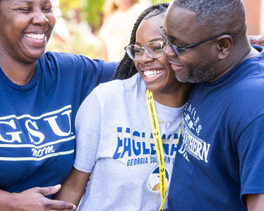 Two proud Georgia Southern parents embrace their student, who's wearing an Eagle Nation T-shirt and lanyard.