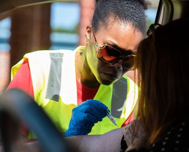 A student from Georgia Southern's Jiann-Ping Hsu College of Public Health wearing sunglasses and a hi-vis vest interacts with a member of the public