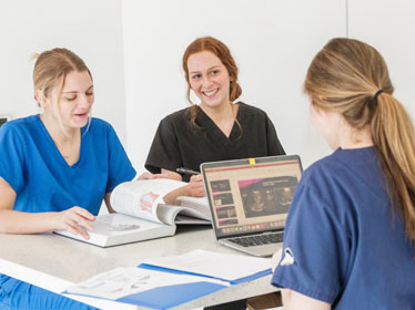 Three students from Georgia Southern's B.S. in Radiologic Sciences program have a discussion around a table with folders and a laptop.