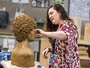 A Georgia Southern Department of Art student sculpts a bust out of clay in an art studio