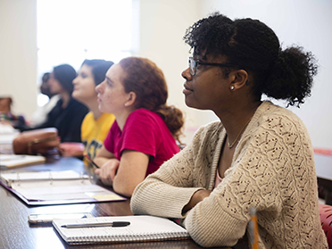 Sitting along a desk, Georgia Southern Department of English students listen to a faculty member's lecture.