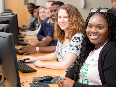 A class of students from Georgia Southern's Department of Information Technology sit by computer monitors in a lab