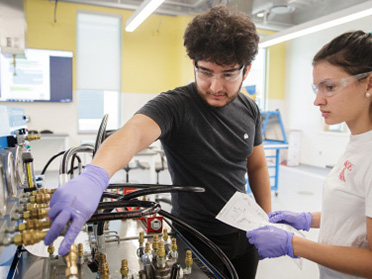 Wearing safety glasses, two students from Georgia Southern's Department of Mechanical Engineering connect hoses to cylinders in a lab