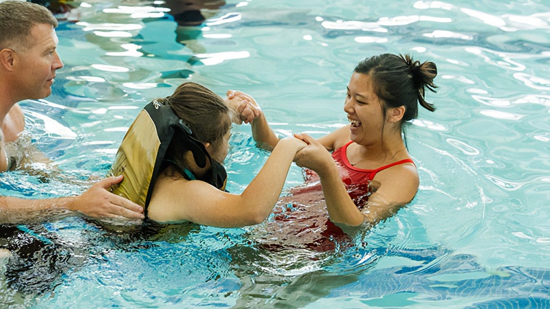 A student helps a child learn to swim.