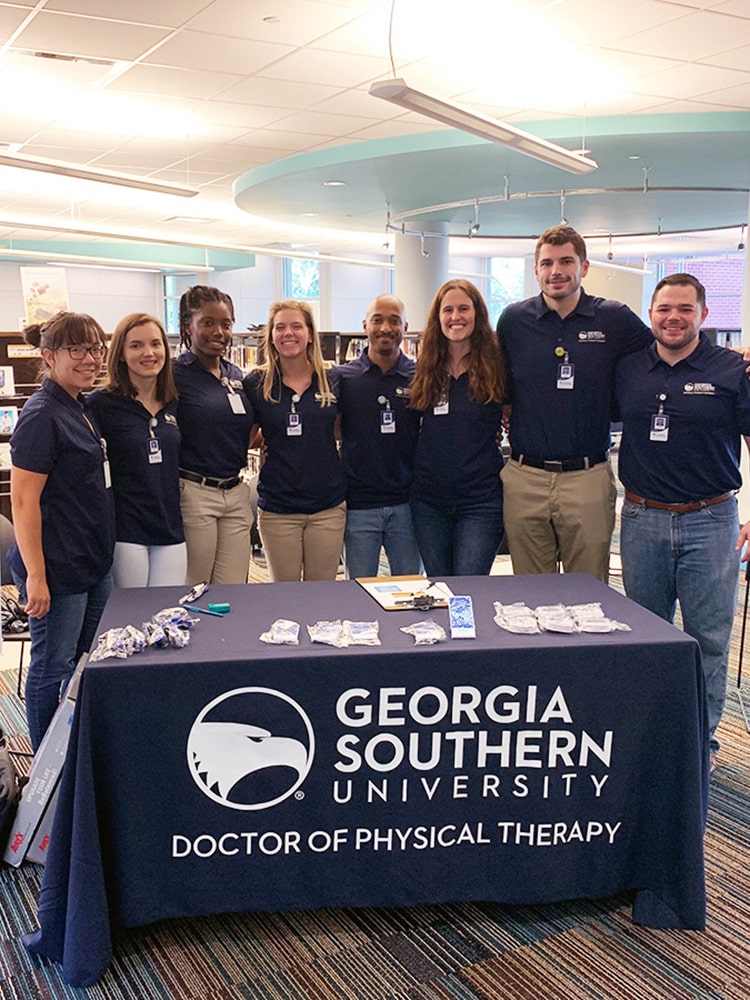 A group of students lock arms as they stand around a table for Georgia Southern's DPT program