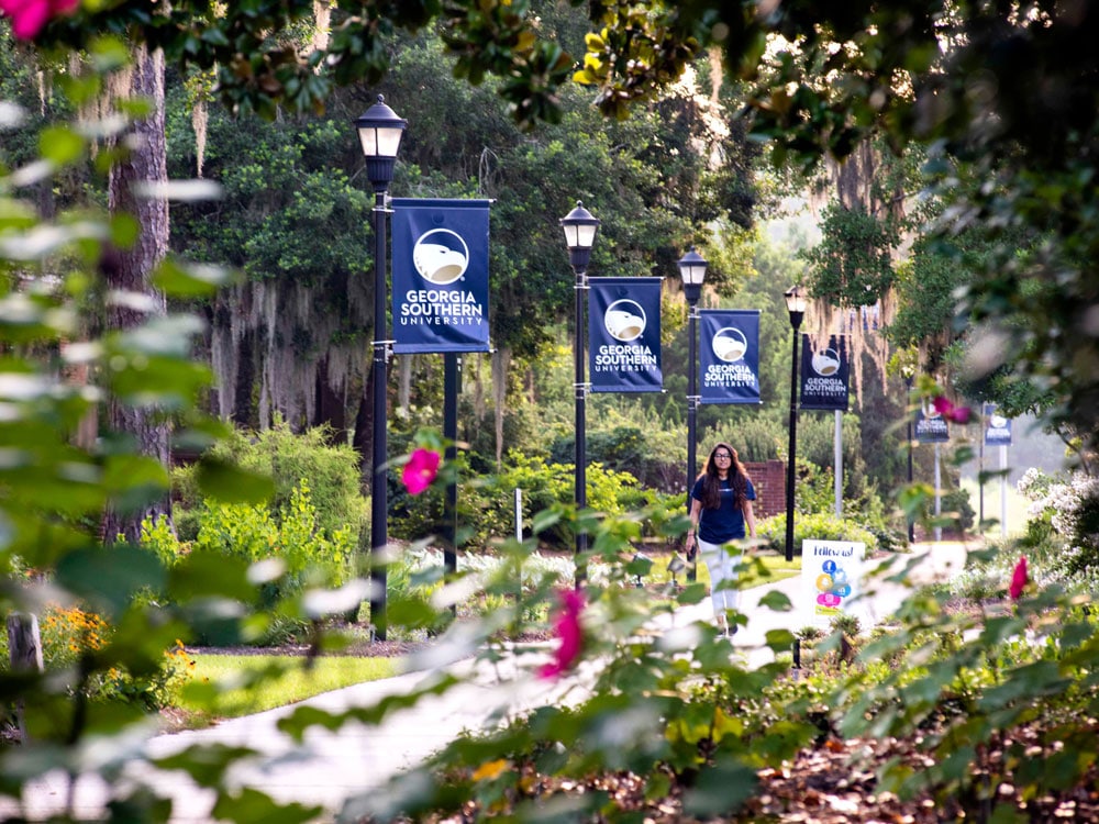 A student walks along a path near banners for Georgia Southern's Armstrong Campus