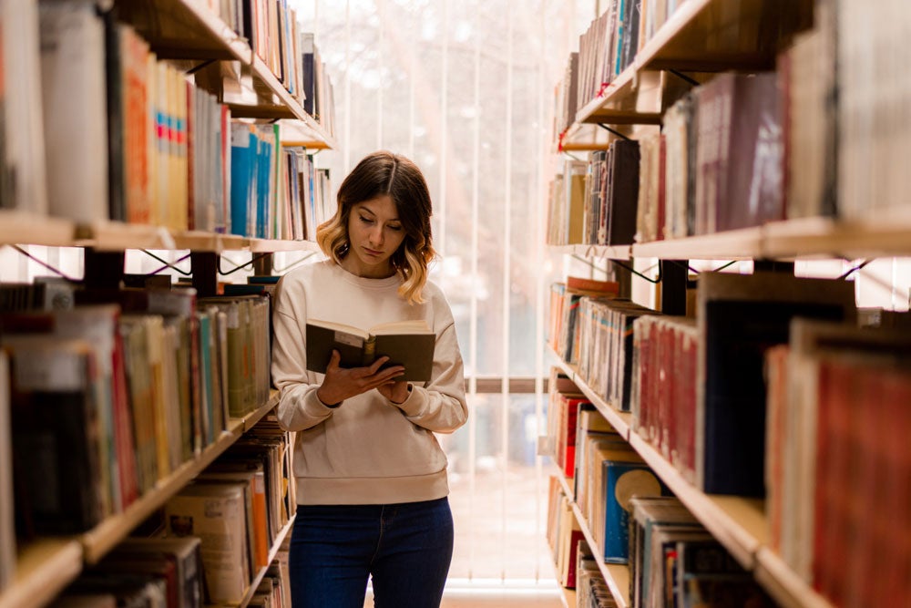 georgia southern student in the library, reading a book amongst multiple available resources on the shelves