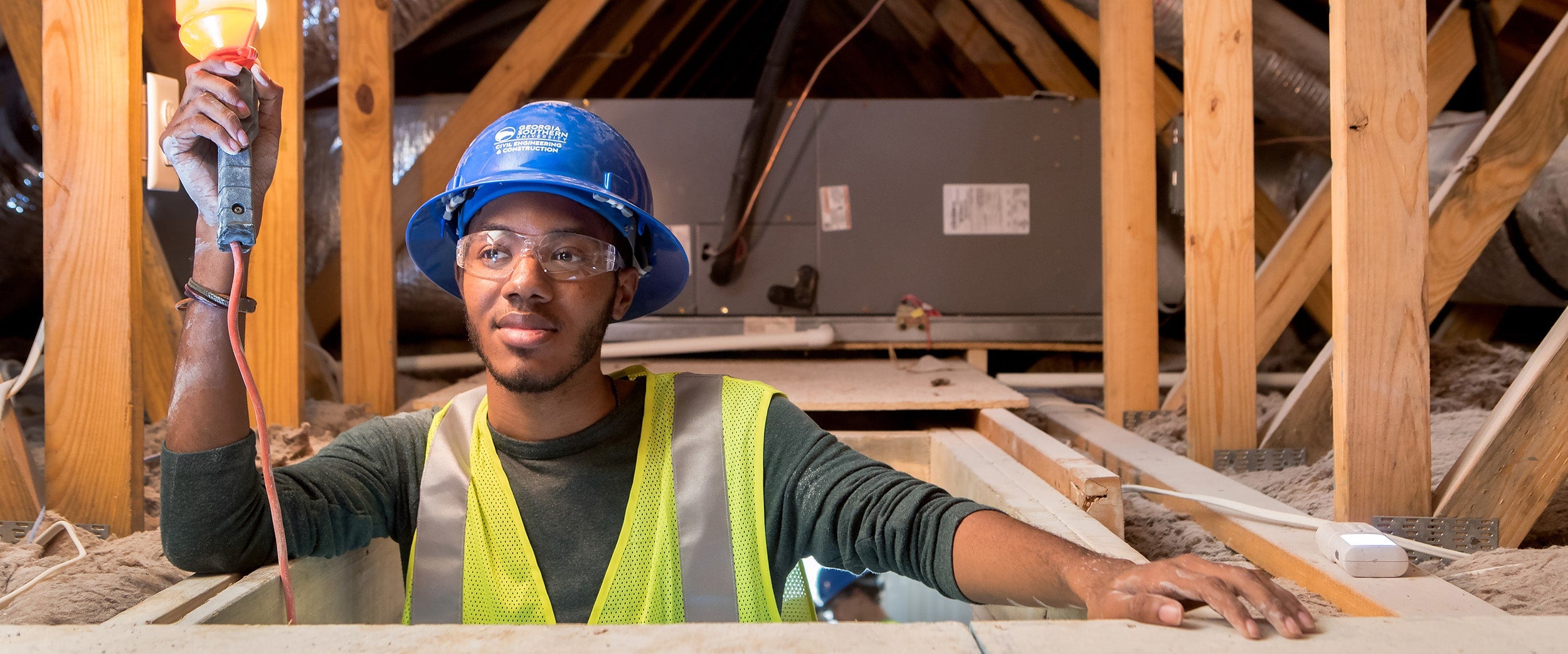 Georgia Southern student climbing into an attic with a light.