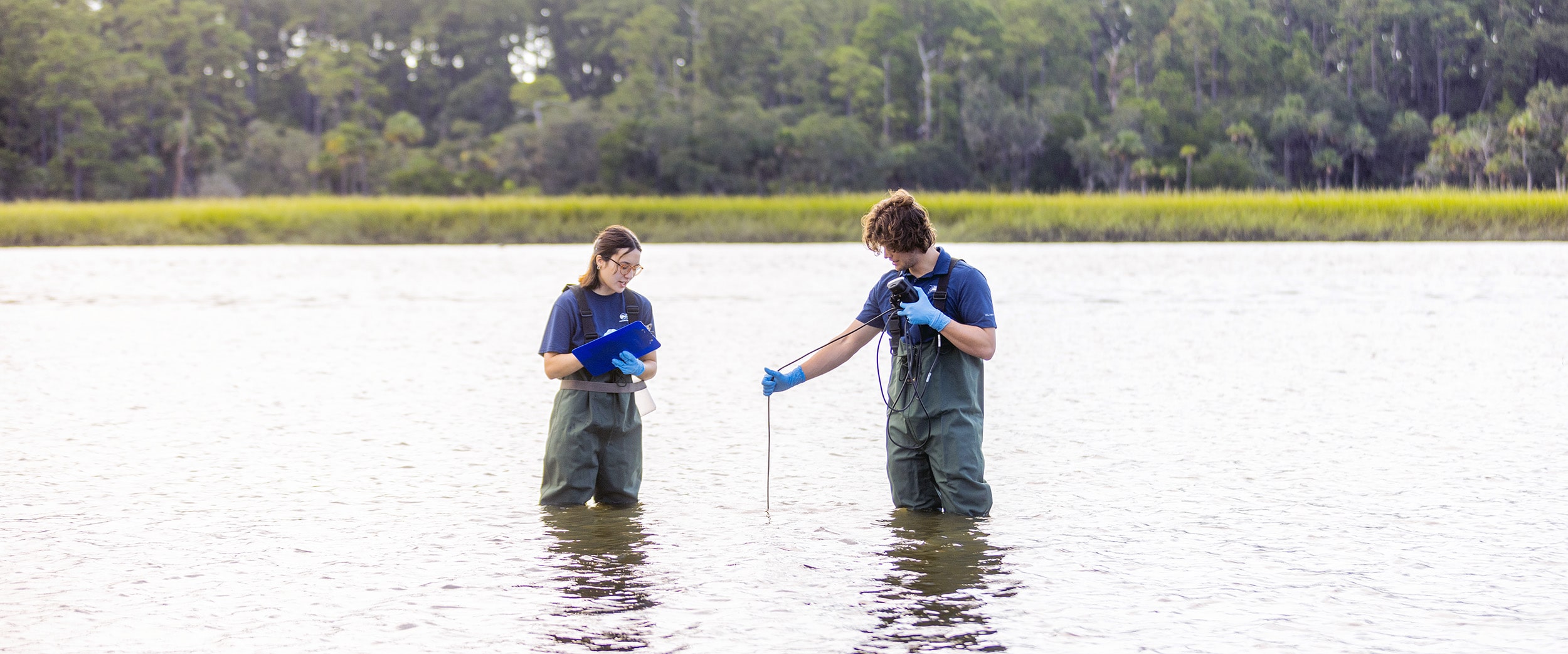 Two students stand in a body of water collecting data for research