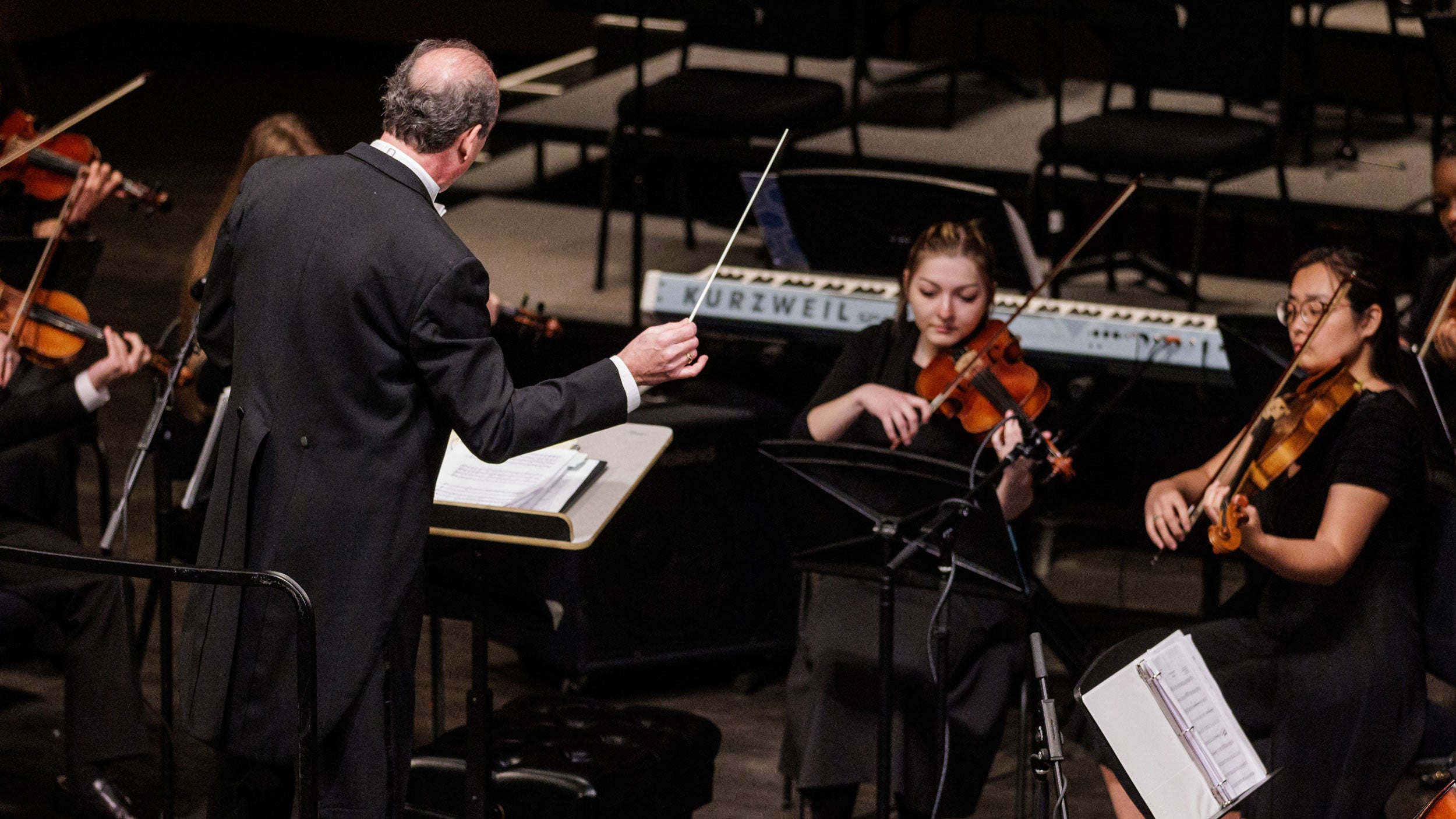 A group of Georgia Southern students in an academic concert hall all playing the violin. Students are sitting in front of the conductor.