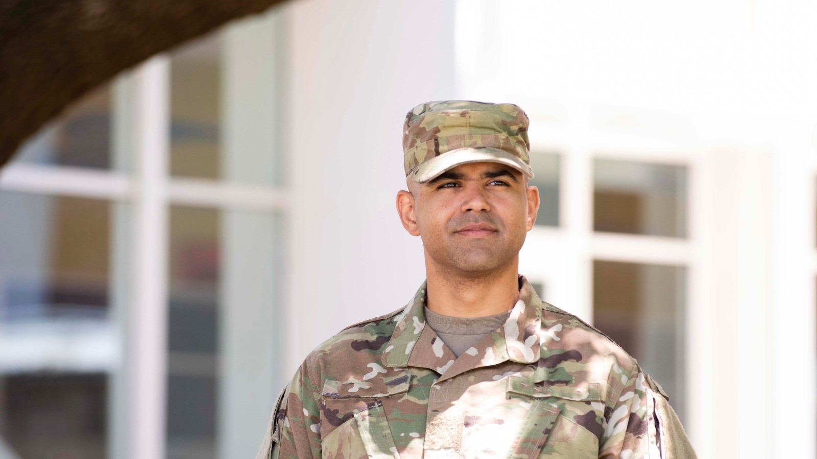 A soldier in combat uniform gazes pensively into the distance.