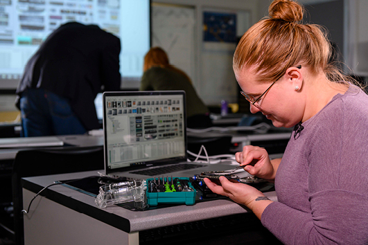 A student from Georgia Southern's M.S. in Electrical and Computer Engineering program examines computer hardware connected to a laptop