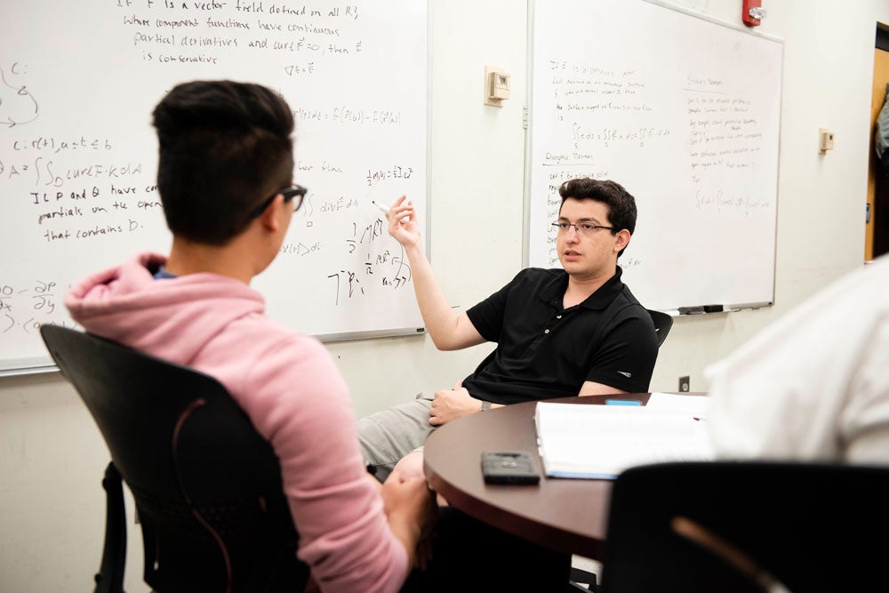 Two students from Georgia Southern's M.S. in Mathematics program debate an equation written on a whiteboard