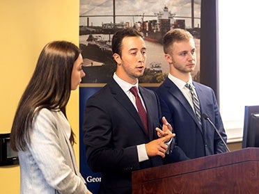 Standing behind a podium, three BBA in Economics students in suits discuss their research to an audience of Georgia Southern students