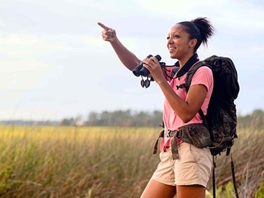 A biology major participating in Georgia Southern's Biological Survey uses binoculars while walking through local wetlands