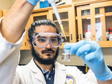 A student uses a pipette to add something to a vial containing liquid.