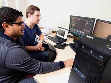 One person working with computer code while another watches