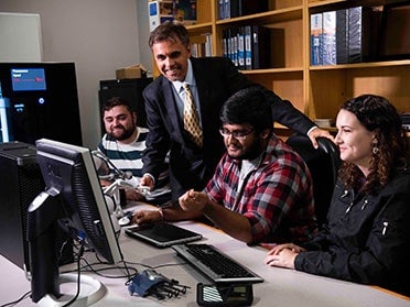 A professor assists three Georgia Southern B.S. in Computer Science students with a paid project for an industry partner