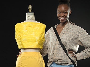 A Georgia Southern B.S. in Fashion Merchandising and Apparel Design student stands with her creation, a two-piece yellow outfit on a dress form, during Fashion Menagerie