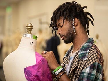 In a design studio at Georgia Southern, a student pins the bust of a pink polka dot dress to a dress form