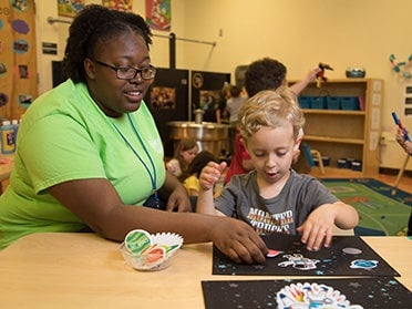 A B.S. in Human Development and Family Science student from Georgia Southern helps a preschool-age child put together a 2-D outer space scene