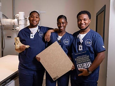 Three B.S. in Radiologic Sciences, Diagnostic Medical Sonography students at Georgia Southern proudly show off course materials in an on-campus clinical space.