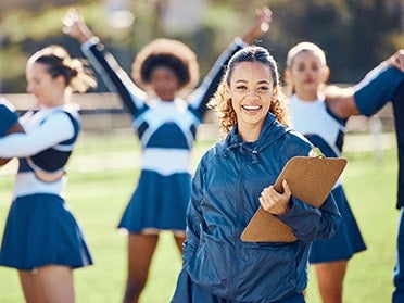 A student from the B.S. in Sport Management program stands with a clipboard near Georgia Southern's cheerleading team