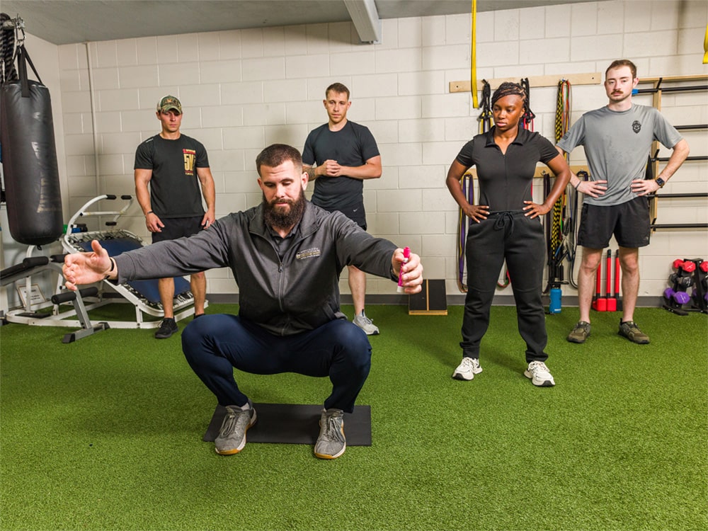 An athlete performs a squat-like maneuver as volunteers for Georgia Southern's Tactical Athlete Initiative observe