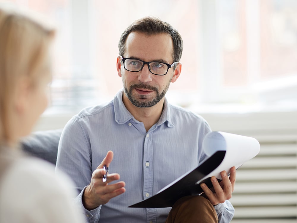 A man holding a clipboard and speaking to a woman in the foreground