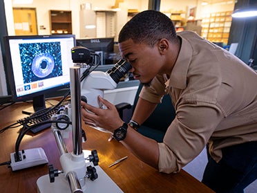 Sitting in front of a computer, a student from Georgia Southern's M.A. in Social Science program looks through a microscope.