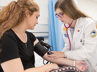 A Georgia Southern MPH student in a lab coat takes a patient's blood pressure during a practicum assignment