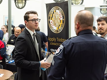 Georgia Southern student, wearing a business suit and speaking with an in-uniform police officer.