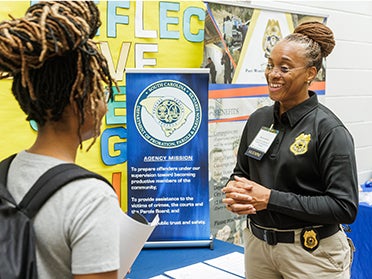 A representative from Georgia Southern's Justice Studies Club stands in front of a booth to talk to a new member