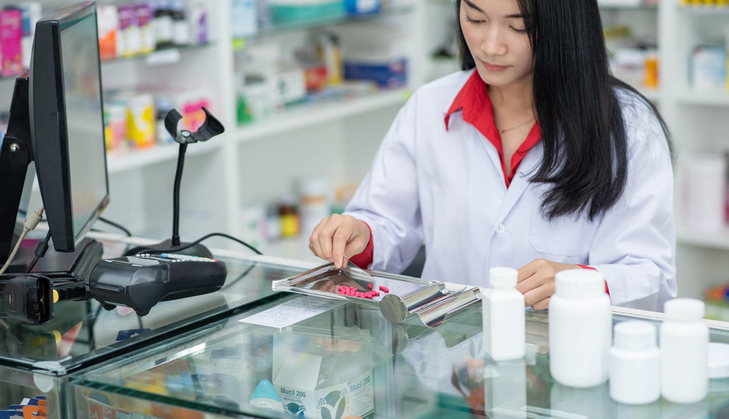 Pharmacist separating pills behind the counter in a phamacy.