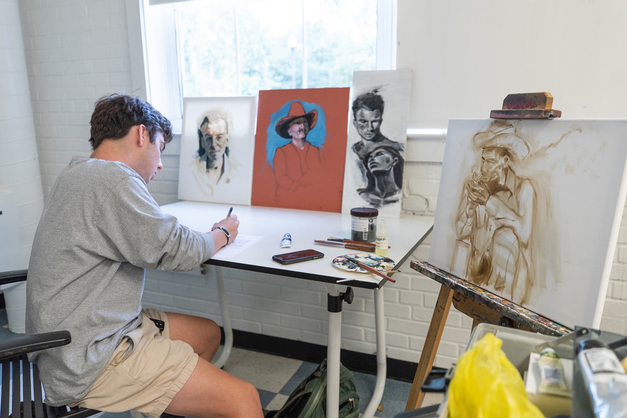 A BFA in Studio Art student in one of Georgia Southern's art studios turns to write while working on a painting of a cowboy