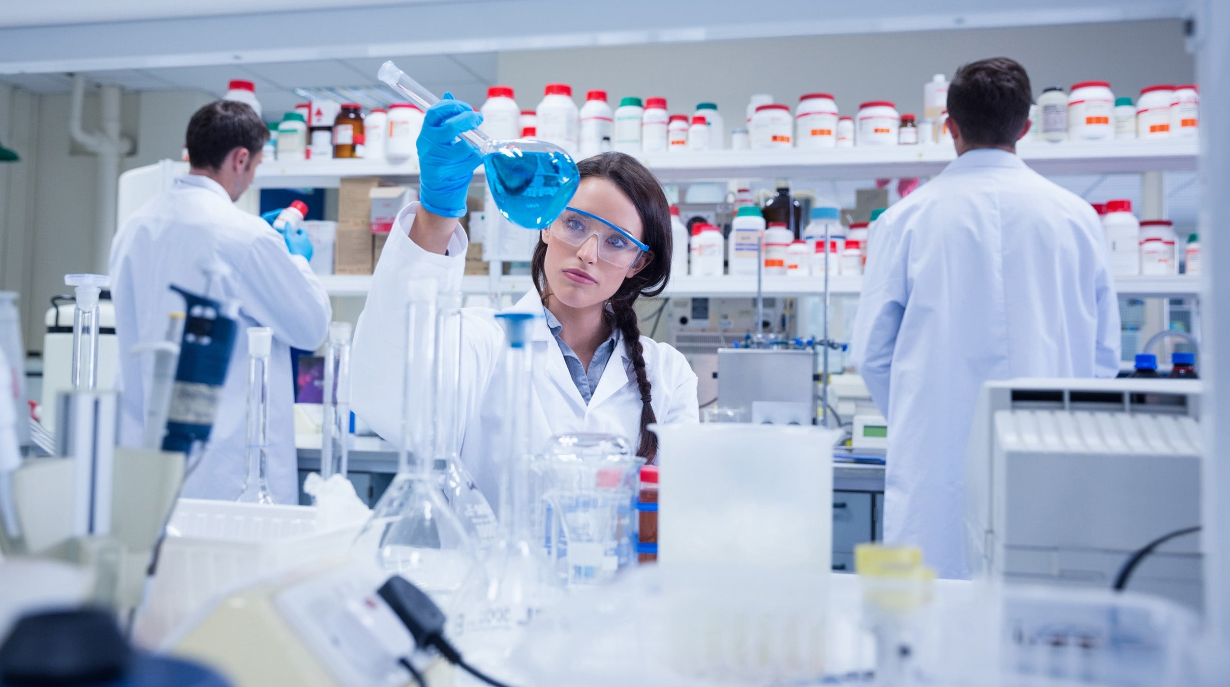 Georgia Southern biochemistry student studying a blue liquid through a volumetric flask.