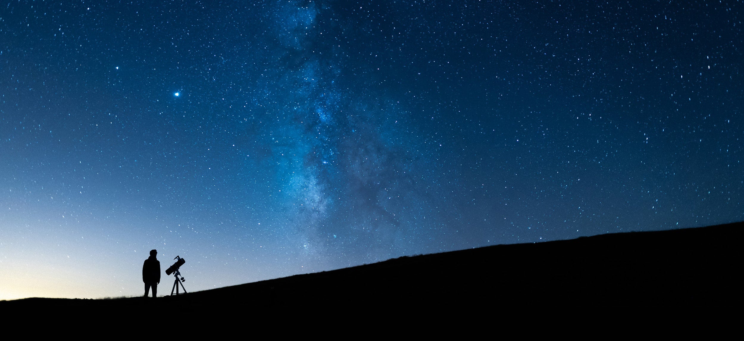 Georgia Southern physics student with a telescope, beneath a starry sky.